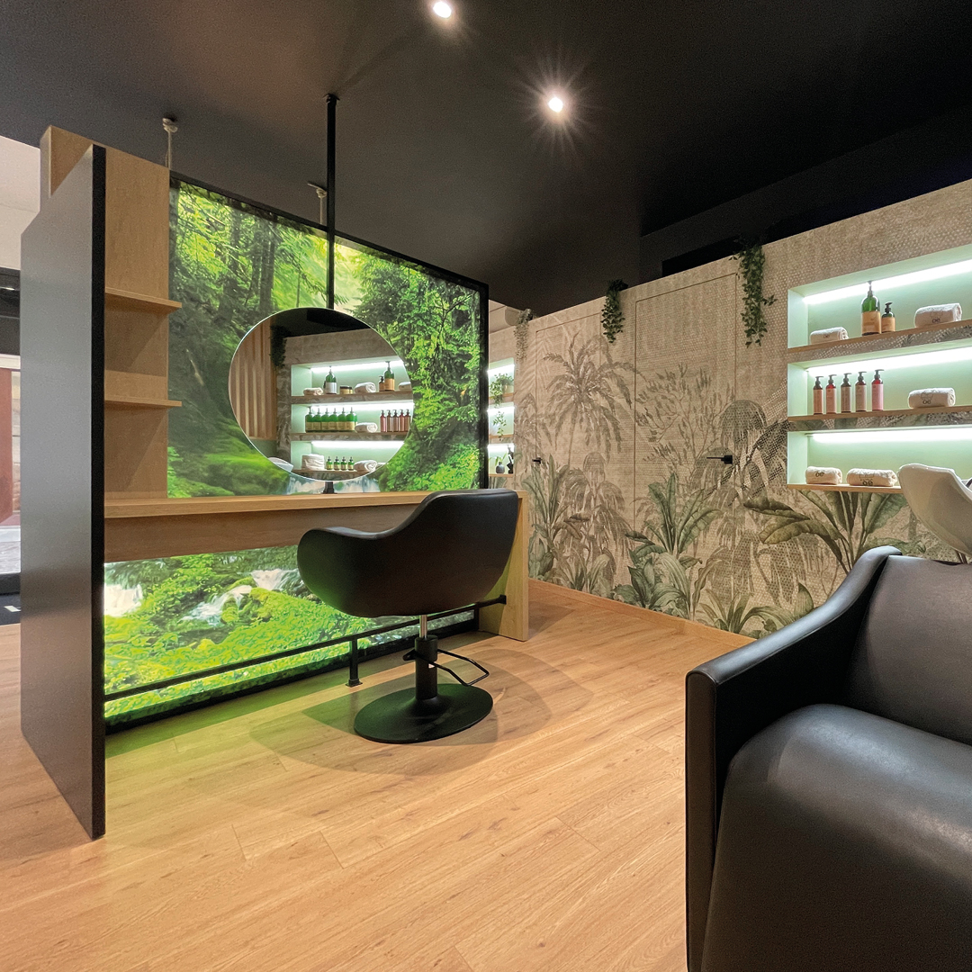 Immagine postazione area stilistica. Specchio a finzione anche decorativa, elementi naturali verdi, mobili in legno e poltrona nera 